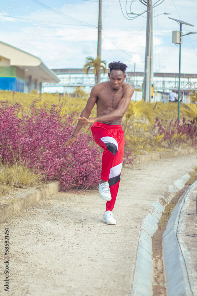 Obraz premium Joven afro bailando al estilo urbano sin camiseta, con hermosa vegetacion y cielo de fondo
