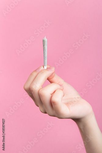 A woman's hand holds a joint with medical marijuana with her fingers.  On a pink background