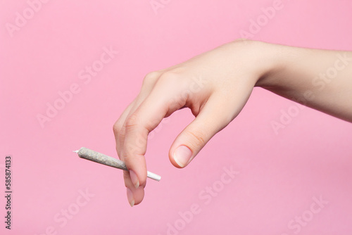 A woman's hand holds a joint with medical marijuana with her fingers.  On a pink background