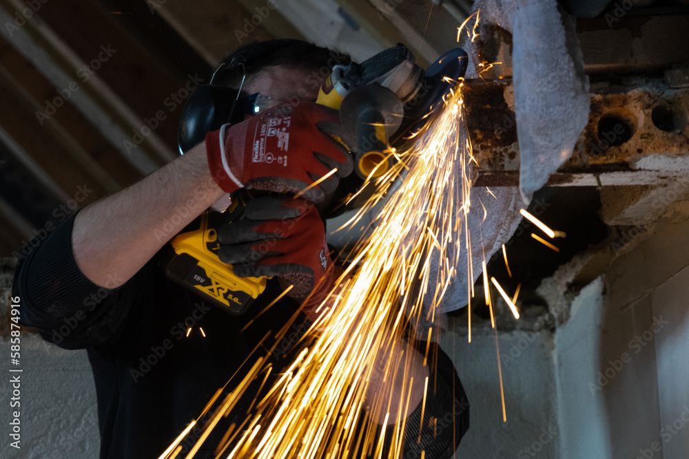 Worker with protective gear working with an angle grinder among flying sparks