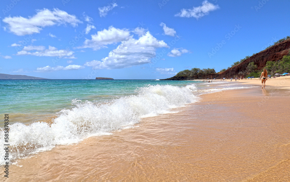 Gold sand beach walker. Blue sea water and dramatic clouds. Maui, Hawaii, USA. Unidentifiable sun bather.
