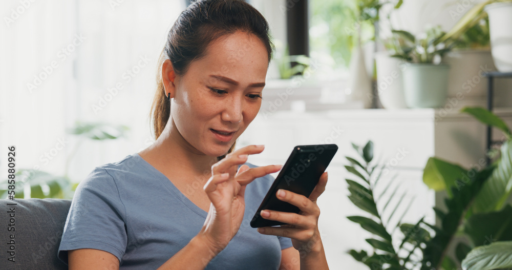 Close-up Young Asian woman wear casual site on couch use smartphone feel exciting scrolling screen online shopping in living room indoor plants at home. Excited and surprised female holding cellphone.