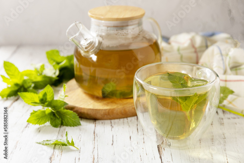 Cup and teapot of fresh natural herbal tea with fresh mint leaves on rustic wooden table. Organic aromatherapy relaxation medical healthy drink.