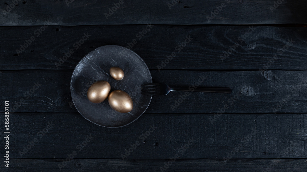 Obraz premium Golden eggs with black fork on black plate on dark background. Easter concept