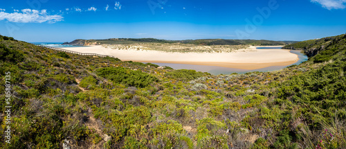 Fototapeta Naklejka Na Ścianę i Meble -  Ultra wide Praia da Amoreira beach with its estuary river Ribeira de Aljezur flowing into the Atlantic Ocean, showcasing crystal clear waters, white sandbanks, dunes and stunning natural landscape.