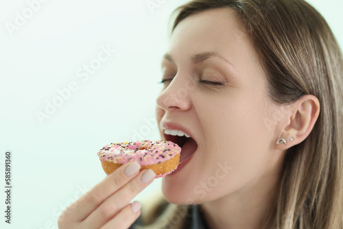 Happy woman bites delicious donut on light background