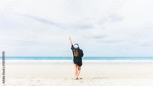 Unrecognizable woman on the beach with a hand in the form of victory to the sky