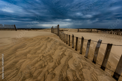 fence on sand dune with clouds