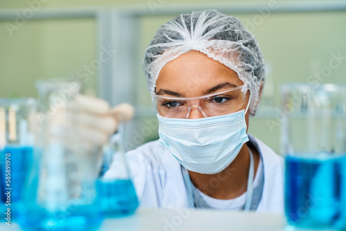 Focus on face of young African American female chemist taking test tube with blue liquid while carrying out scientific experiment in laboratory