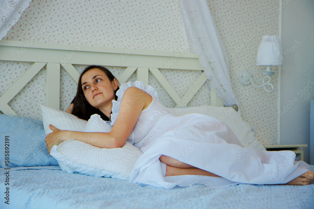 Portrait of young woman in retro-styled nightdress lies on the bed in the bedroom at home