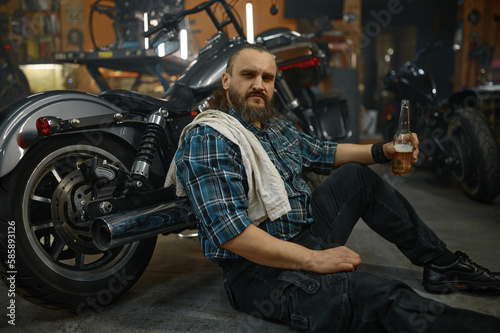 Exhausted mature man biker sitting on floor holding opened glass of beer