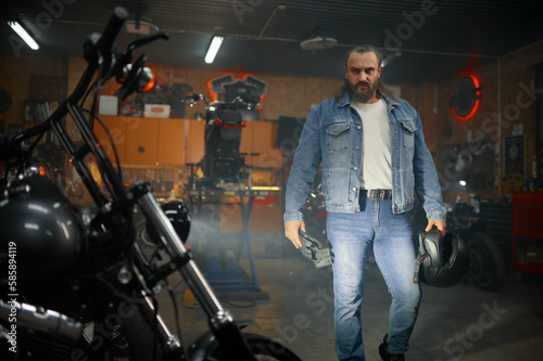 Portrait of bearded brutal biker looking motorcycle in garage workshop