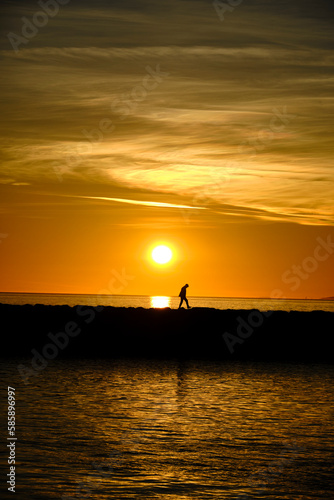 person crossing the sea under a sunset