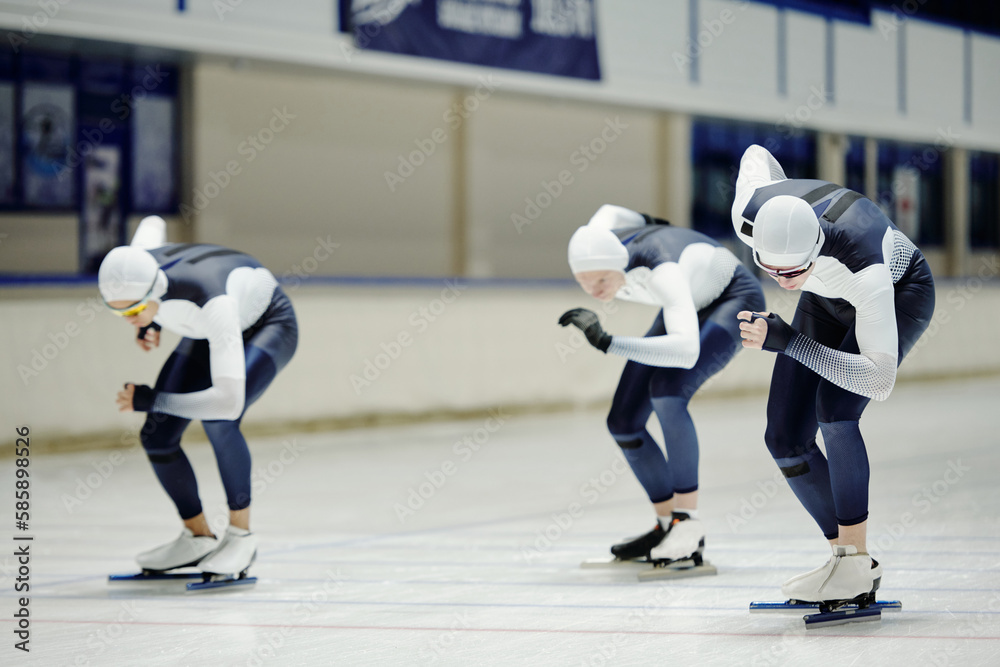 Fototapeta premium Group of fit youthful sportsmen in sports uniform sliding along ice rink in large modern arena taking part in short track speed skating race