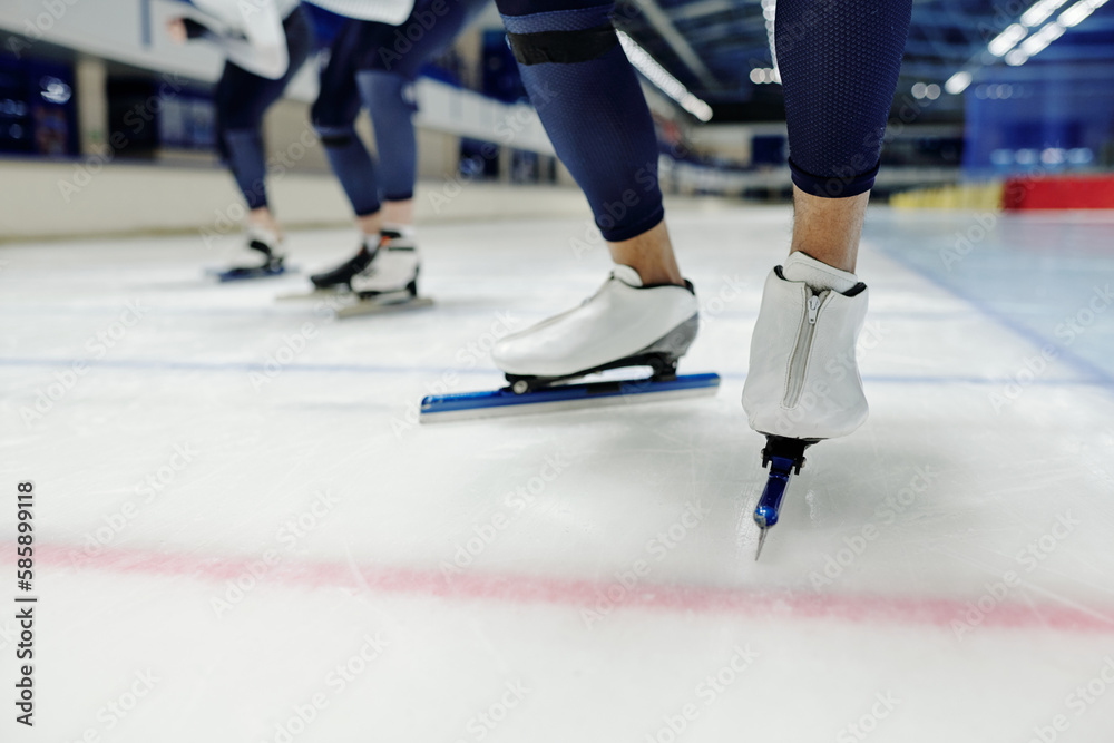 Close-up of lower part of legs of young sportsman in skates taking part in speed skating competition sliding forwards along ice rink