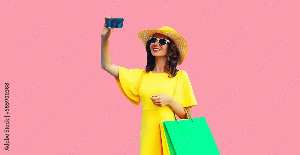 Beautiful happy smiling woman taking selfie by smartphone with shopping bags wearing yellow dress, summer straw hat on colorful pink background Beautiful happy smiling woman taking selfie by smartphone with shopping bags wearing yellow dress, summer straw hat on colorful pink background
