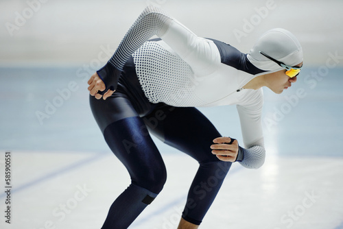 Young active man in speed skating uniform and eyeglasses bending forwards while practicing one of exercises during training photo