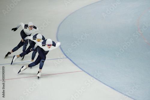 Row of three young active athletes on skates sliding along ice rink while practicing some exercises during training before competition