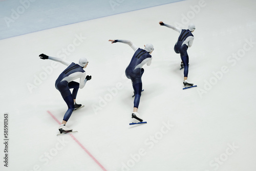 High angle of three young men in sports uniform and skates moving forwards along ice rink during short track speed skating competition
