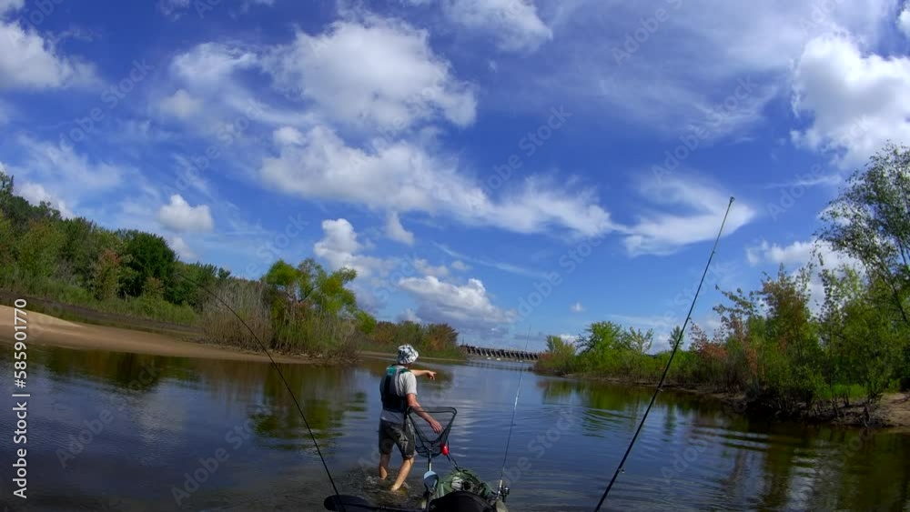 Wide angle point of view shot of man pulling his fishing kayak while going upstream through shallow water.