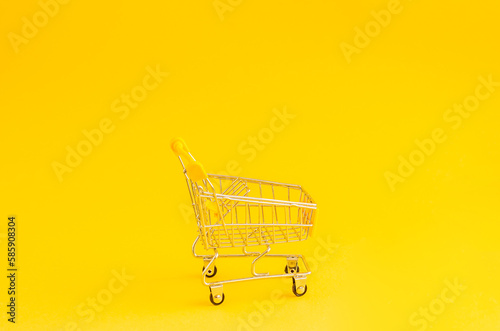 Miniature shopping trolley on a yellow background with place for text.