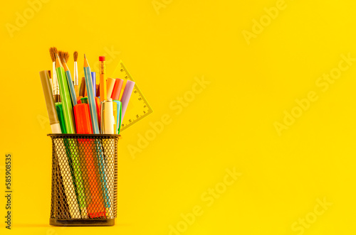 Black cup with items for school on a yellow background with place for text.