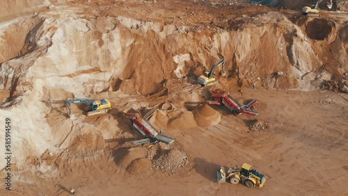 Quarry dump truck unloads the rock into a rock crusher. Open pit mine quarrying extractive industry stripping work. Conveyor and production of construction gravel and sand.
