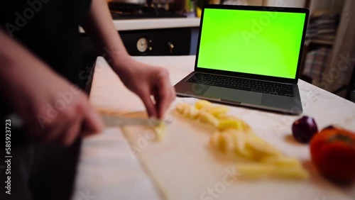 Close-up of a young woman cutting vegetables and searching for a recipe on her laptop with chroma key