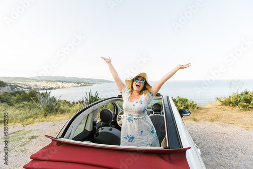 Happy woman sitting in white convertible car with beautiful view and having fun - travel summer vacation and rental car concept