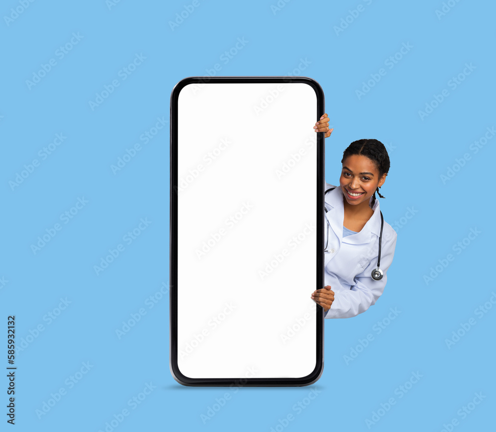 Medical App. Smiling Black Doctor Lady Peeking Out Behind Big Blank Smartphone Medical App. Smiling Black Doctor Lady Peeking Out Behind Big Blank Smartphone