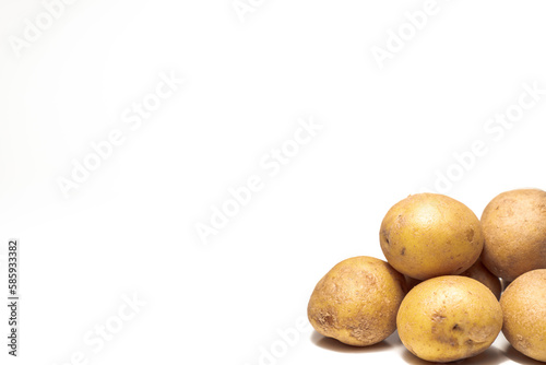 A close up photograph of a pile of yellow and brown russet potatoes in lower right corner with white background and copy space. photo