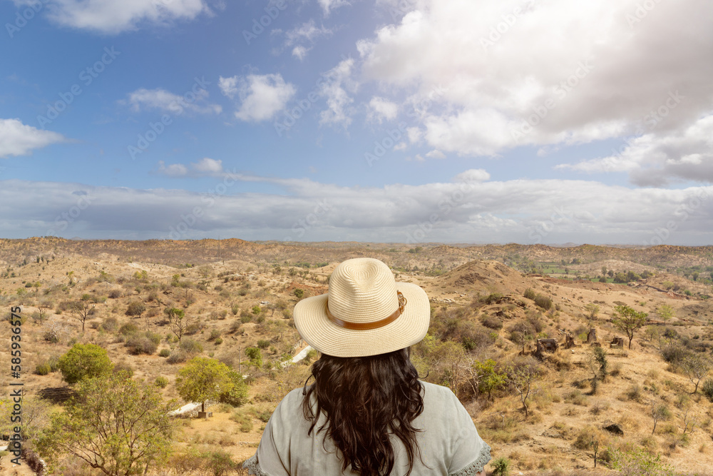woman with straw hat stands with her back to the camera and looks into a steppe-like landscape