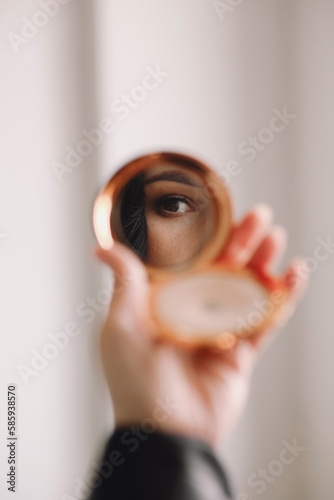 Female hand holding small mirror with reflection of girl's eye isolated over white background. Concept of beauty, creativity and ad