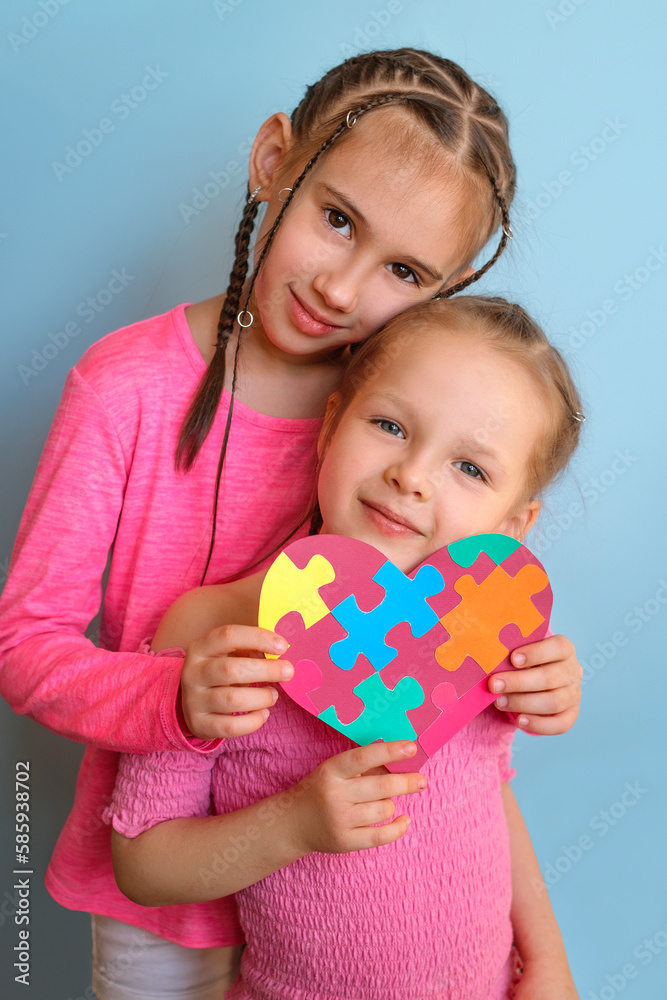 Cute sisters with pigtails look with a smile at the camera holding the autism symbol in their hands. Caring for each other, love and support of loved ones and relatives Cute sisters with pigtails look with a smile at the camera holding the autism symbol in their hands. Caring for each other, love and support of loved ones and relatives