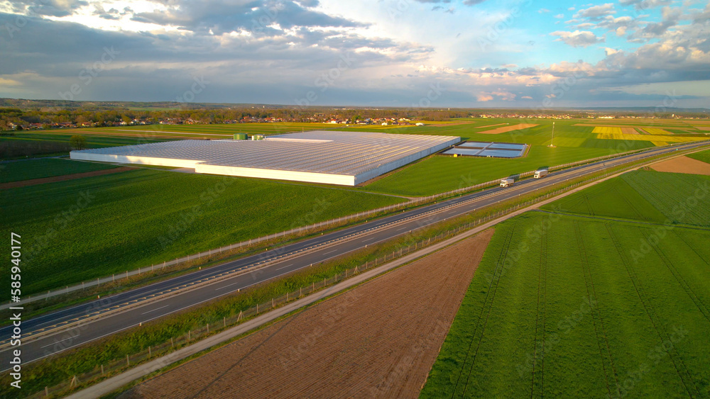 AERIAL Big greenhouse for vegetable production near highway road in golden light