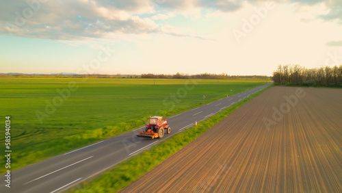 AERIAL: Red tractor with attached farming machinery driving on countryside road