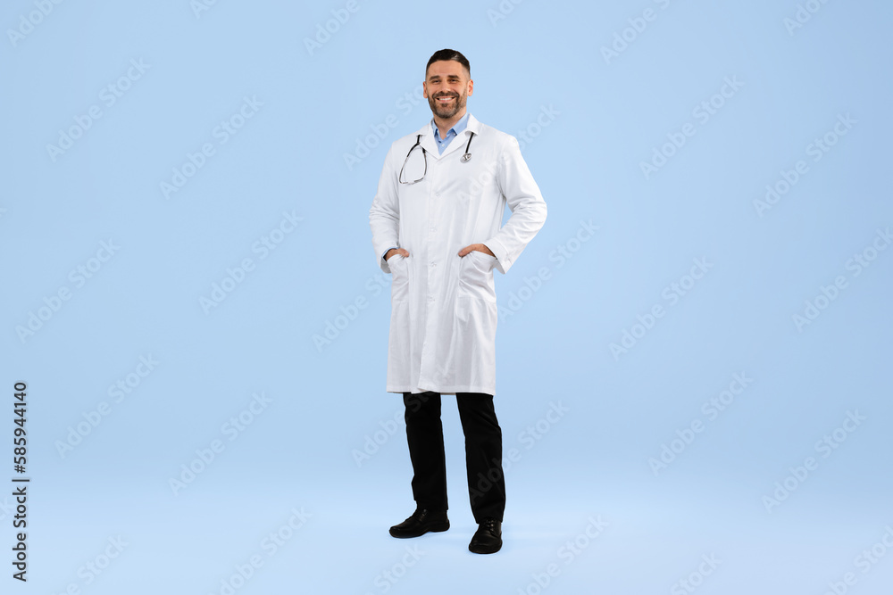 Confident middle aged male doctor in white coat posing with hands in pockets on blue background, full length Confident middle aged male doctor in white coat posing with hands in pockets on blue background, full length