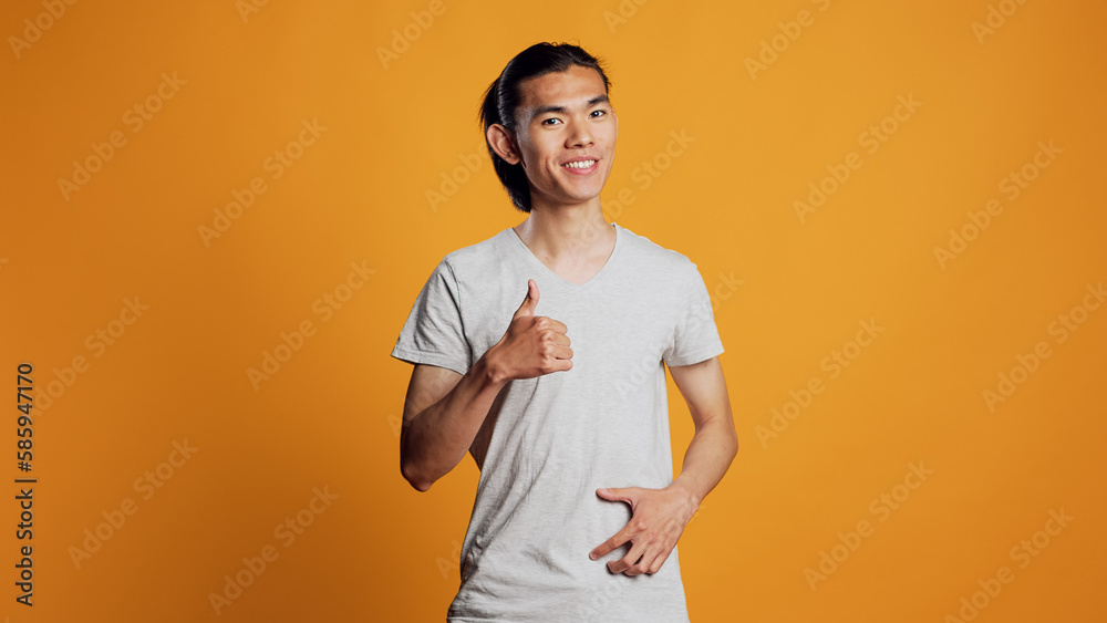 Positive man giving thumbs up in studio, expressing approval and good vibes. Happy male model acting cheerful and showing like or agreement, good symbol and success on camera. Positive man giving thumbs up in studio, expressing approval and good vibes. Happy male model acting cheerful and showing like or agreement, good symbol and success on camera.