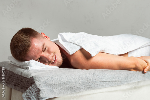 A happy, satisfied client is lying on their stomach on a massage table during a massage.