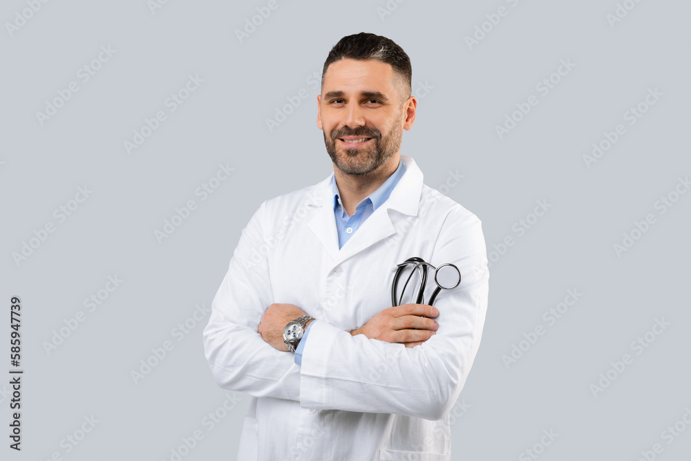 Confident male medical practitioner in white coat holding stethoscope in hand, posing with folded arms Confident male medical practitioner in white coat holding stethoscope in hand, posing with folded arms
