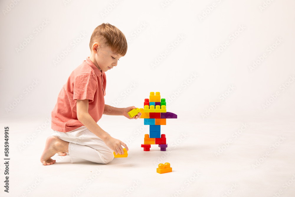 A happy child collects a tower of colored cubes. The preschooler sits down at the white background and assembles the construction set. The boy smiles, pleased with the result. A happy child collects a tower of colored cubes. The preschooler sits down at the white background and assembles the construction set. The boy smiles, pleased with the result.