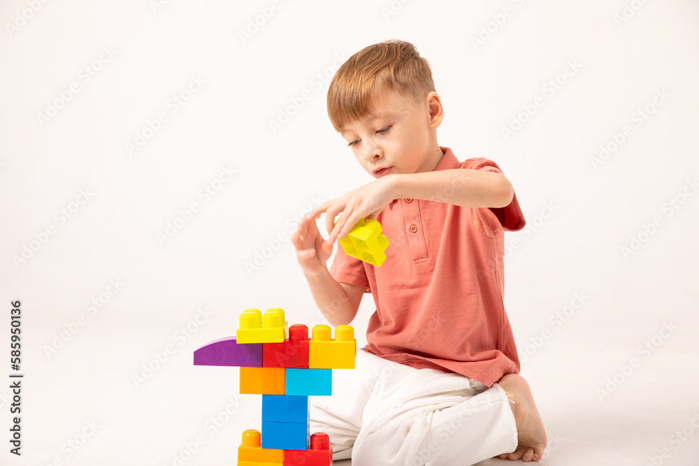 A happy child collects a tower of colored cubes. The preschooler sits down at the white background and assembles the construction set. The boy smiles, pleased with the result. A happy child collects a tower of colored cubes. The preschooler sits down at the white background and assembles the construction set. The boy smiles, pleased with the result.