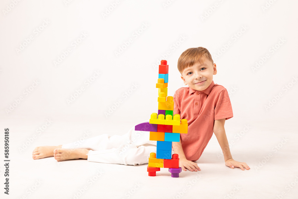 A happy child collects a tower of colored cubes. The preschooler sits down at the white background and assembles the construction set. The boy smiles, pleased with the result. A happy child collects a tower of colored cubes. The preschooler sits down at the white background and assembles the construction set. The boy smiles, pleased with the result.