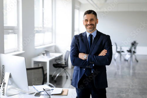 Successful business person. Portrait of male entrepreneur standing in office, posing with folded hands smiling at camera