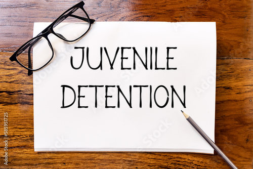 Juvenile detention text on blank notebook paper on wooden table with pencil and glasses aside. Business concept and legal concept about juvenile detention.