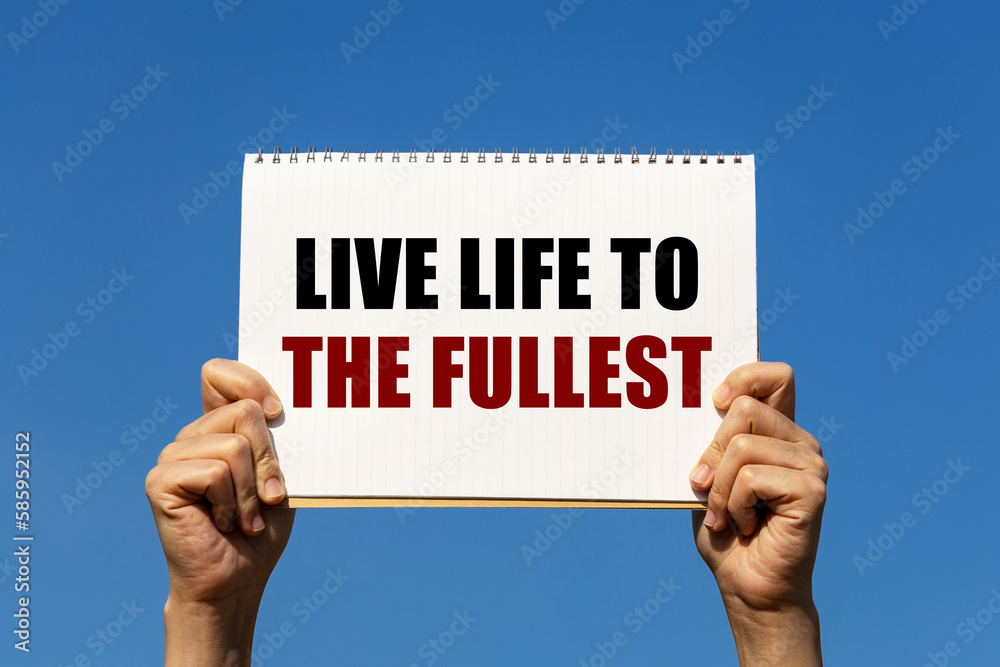 Live life to the fullest text on notebook paper held by 2 hands with isolated blue sky background. This message can be used as business concept about live life to the fullest. Live life to the fullest text on notebook paper held by 2 hands with isolated blue sky background. This message can be used as business concept about live life to the fullest.
