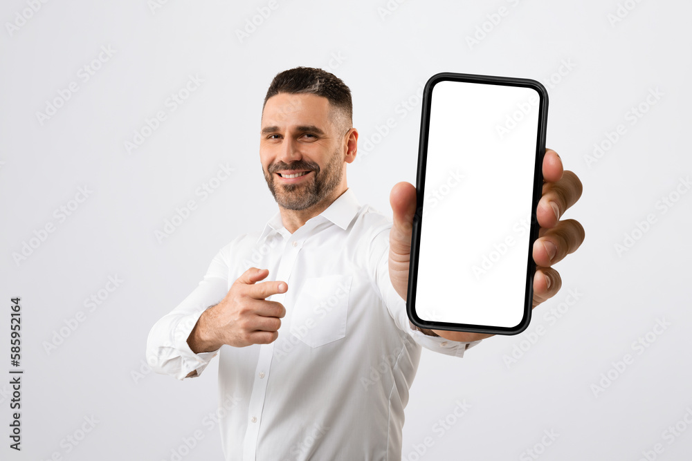 Positive male entrepreneur pointing at giant blank smartphone screen, recommending new mobile app or website, mockup