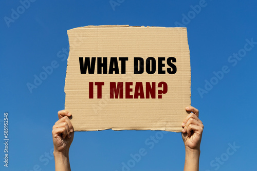 What does it mean text on box paper held by 2 hands with isolated blue sky background. This message board can be used as business concept to ask audience what does it mean. photo