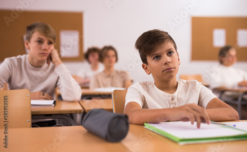 Portrait of upset tired teenage schoolboy sitting in classroom secondary school, learning lessons