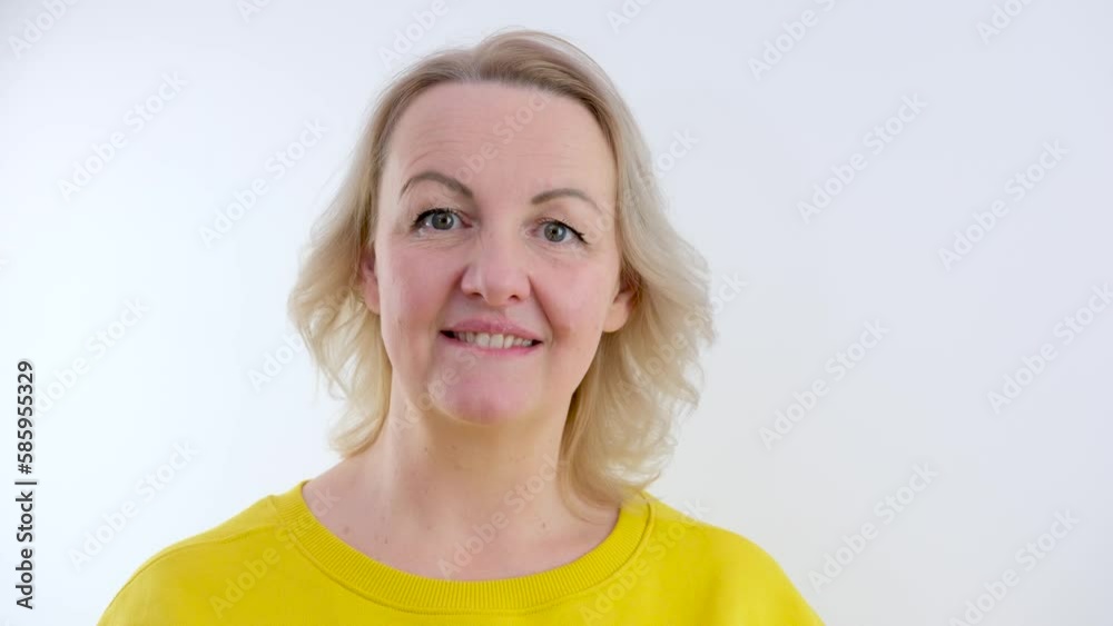 woman agrees shakes head looks at the camera shrugs shoulders smiling squints her eyes blond hair yellow clothes on a white background bit her lower lip turned away smiled makes her eyes